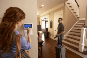 Woman adjusting thermostat as husband walks away with suitcase
