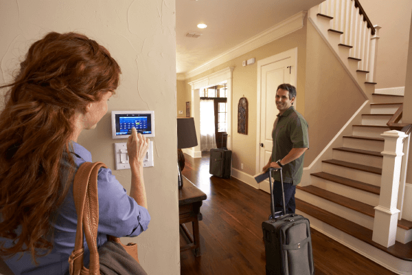 Woman controls thermostat while man with suitcase prepares to leave home